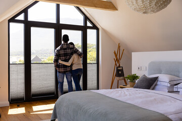 African american couple embracing looking out window in bedroom
