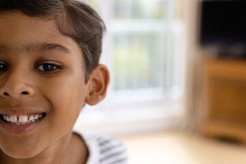 Half portrait of happy biracial boy smiling in bedroom at home, copy space