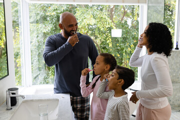 Happy happy biracial parents, son and daughter brushing teeth together in bathroom in the morning