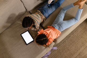 Overhead of biracial brother and sister lying on couch using tablet with copy space on screen