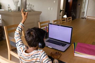 Biracial boy using headphones and laptop with copy space for online lesson at home raising hand