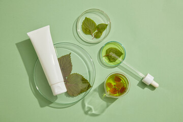 A podium with beauty container placed on. Essential oil and beefsteak leaves is contained inside petri dishes and beaker. Natural product advertising of Beefsteak Plant (Perilla frutescens) extract