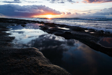 Golden hour on beach. Close up shot of reflection in water. Dramatic sea sunrise. Burning sky and shining golden waves. Reflection of sunlight over water surface.