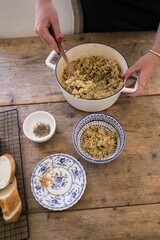 Young adult female cooking in a kitchen, stirring a pot of rice served with baguettes