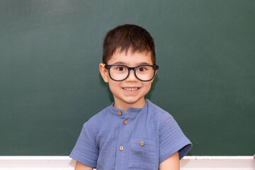 preschooler boy kid happy in front of blackboard writing numbers with white chalk.happy smart child with glasses frame on eyes. back to school concept.free space for text
