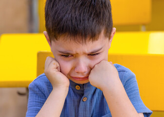 cute preschooler boy crying in classroom or outside with backpack in hands.dissatisfied unhappy sad...