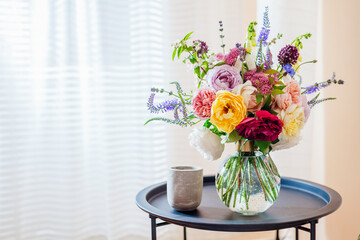 Close up of summer bouquet of roses flowers in transparent vase on table. Interior and decor at home. Space