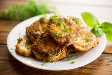 zucchini fried in circles in batter with herbs, in a plate .