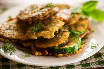 zucchini fried in circles in batter with herbs, in a plate .