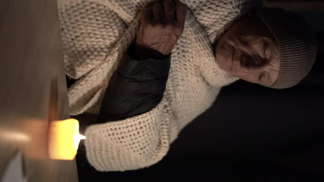 Shutdown of heating and electricity, power outage, blackout, load shedding or energy crisis. Mature man hands warm on candle at home.