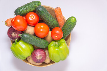 Topview of vegetables (tomatoes, potatoes, onions, cucumbers, carrots) in a bowl on a white background