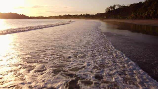 Aerial of the foamy sea hitting the Playa Carrillo beach during the bright sunset in Costa Rica