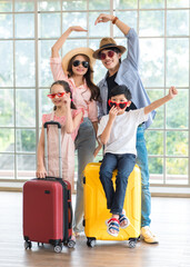 Fototapeta na wymiar Asian cheerful happy family mom dad son and daughter wearing sunglasses and hat standing posing with two trolley luggages smiling celebrating holiday together ready for traveling vacation road trip