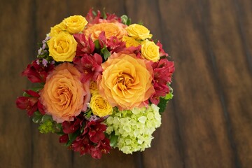 Top view of a stunning floral arrangement of warm-colored roses on a rustic brown wooden table