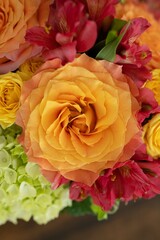 Close-up top view of beautiful orange roses, with red flowers and green hydrangeas in the background