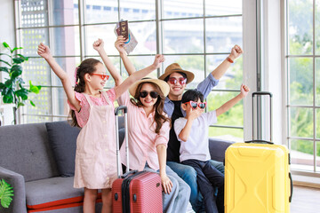Asian cheerful happy family mom dad son and daughter wearing sunglasses and hat with two trolley luggages raising hands smiling celebrating holiday together ready for traveling vacation road trip