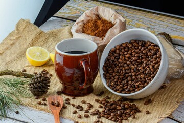Ceramic mug with coffee, a bowl of coffee beans and a bag of seasoning on a burlap sack