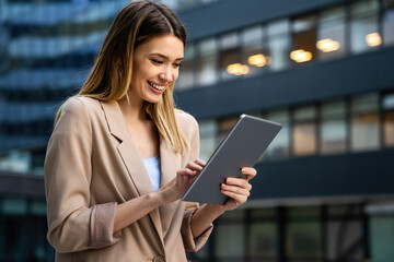 Successful businesswoman using a digital tablet while standing in front of business building.