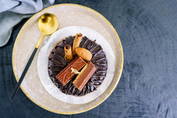 Brown chocolate cake with toppings on plate with spoon on black wooden background.