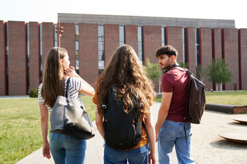 Back view of three caucasian students walking through university campus