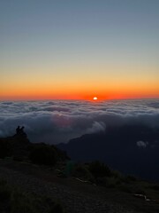 Group of people stands on high cliff overlooking the horizon with the sun setting in the background