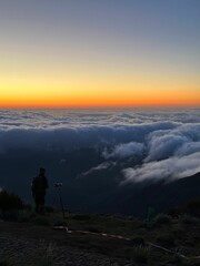 Person standing atop a hill, overlooking the horizon with the sun setting in the background