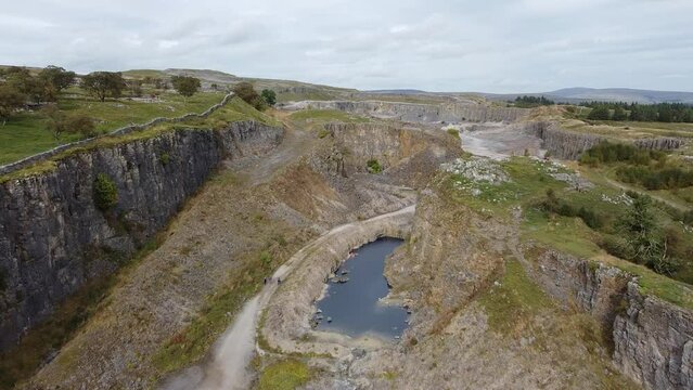 Aerial footage over green hills valley with small pond and cloudy sky on the horizon