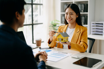Asian Real estate broker agent presenting and consult to customer to decision making sign insurance form agreement, home model, concerning mortgage loan offer in office