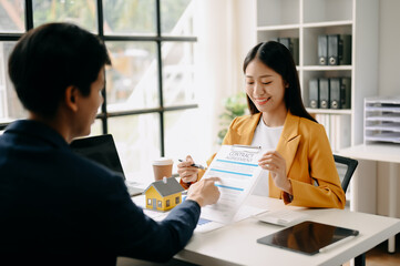 Asian Real estate broker agent presenting and consult to customer to decision making sign insurance form agreement, home model, concerning mortgage loan offer in office