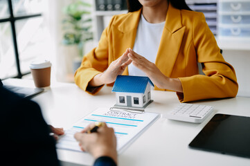 Female real estate agent is use hands to protect red roof for the concept of real estate investment about house trading, purchase at desk .
