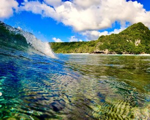 Ocean wave breaking with beach and cliff in background, Guam - obrazy, fototapety, plakaty