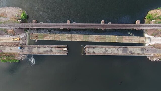 Pontoon bridge of the Ukrainian army. Installation of a temporary crossing near the destroyed bridge. Soldiers collect pontoon ferry. Top view from a drone. 