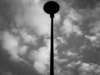 Black and white of street lamp illuminated against a cloudy grey sky