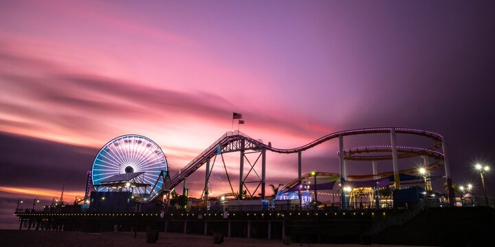 roller coaster and amusement wheel against a sunset sky at night