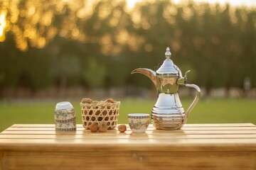 Silver teapot on a wooden table with cups and dried apple on a grassy lawn in sunny outdoor setting
