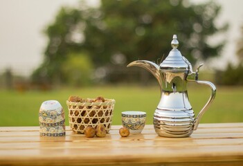 Silver teapot on a wooden table with cups and dried apple on a grassy lawn in sunny outdoor setting