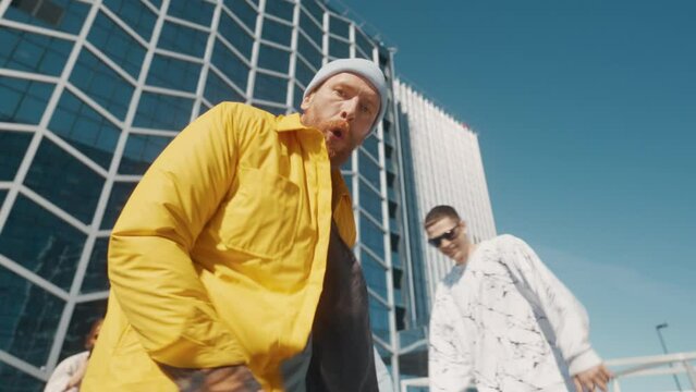 Young And Athletic B-Boy Breakdancing To Break Beats On The City Street In The Circle Of Friends. Group Of Fashionable Young People Supporting Professional Performer, Filming Him On The Smartphone.