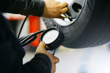 Close up mechanic inflating tire and checking air pressure with gauge pressure in service station