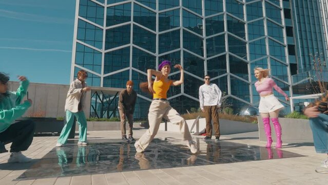 Young And Stylish Female Hip Hop Dancer Improvising On City Street In the Circle Of Fashionable Friends. Group Of Young People Supporting Professional Newstyle Performer, Live Streaming via Smartphone