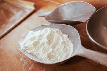 Closeup of a spoons filled with white flour, resting on a rustic wooden