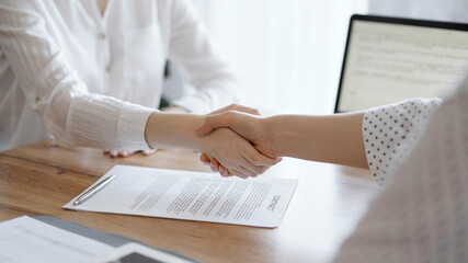 Business people shaking hands above contract papers just signed on the wooden table, close up. Lawyers at meeting. Teamwork, partnership, success concept