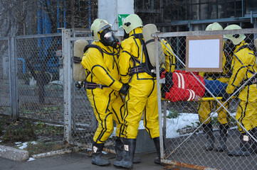 Rescuers in protective rubber suits and masks carrying the sufferer on stratcher from contaminated...