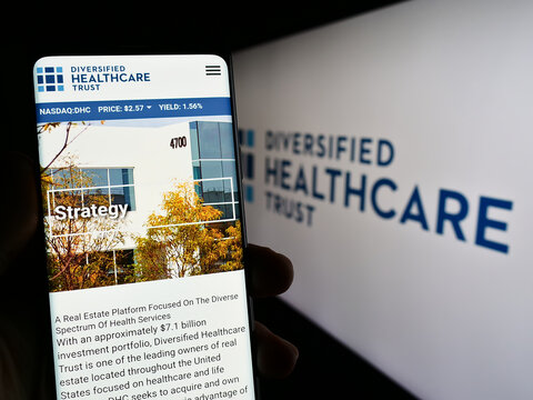 Stuttgart, Germany - 06-18-2023: Person holding mobile phone with webpage of real estate company Diversified Healthcare Trust on screen with logo. Focus on center of phone display.
