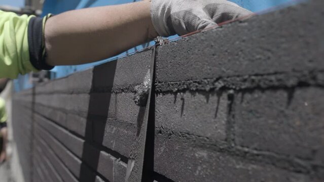 Slow-motion view of a construction worker scraping off excess cement from a brick wall