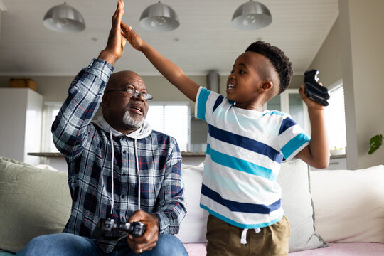 African american grandfather and grandson sitting on sofa and playing video games