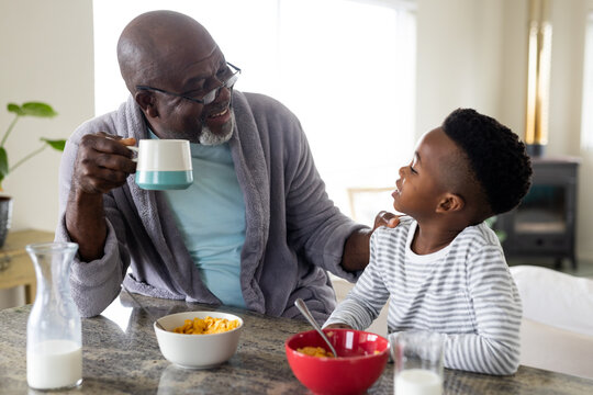 Happy african american grandfather and grandson eating breakfast in kitchen