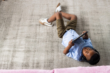African american boy wearing headphones, lying on floor and using tablet