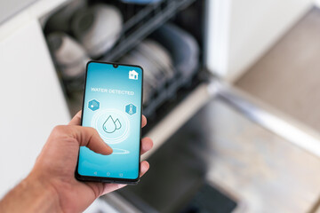 man holding phone with running smart home application, controlling dishwasher remotely. Smart...