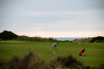Man playing golf on a green field with the sea in the background