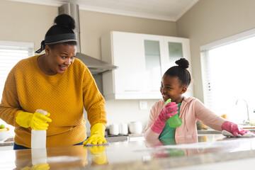 Happy african american mother and daughter cleaning countertop in kitchen